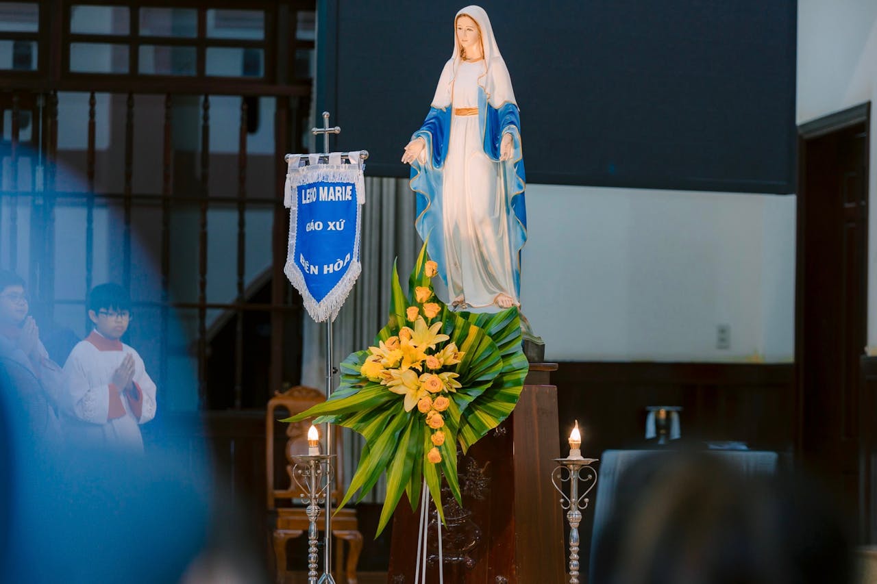 Statue of Virgin Mary at a religious ceremony with candles and flowers indoors.