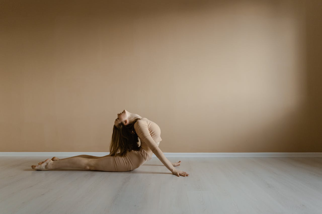 A woman demonstrates a flexible yoga pose in a minimalist indoor environment, embodying peace and balance.